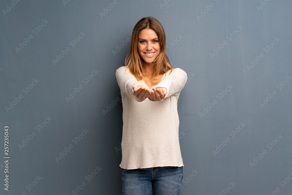 Blonde woman over grey background holding copyspace imaginary on the palm to insert an ad Blonde woman over grey background holding copyspace imaginary on the palm to insert an ad