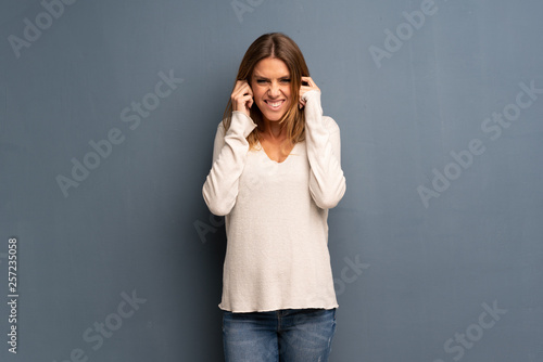 Blonde woman over grey background frustrated and covering ears with hands © luismolinero
