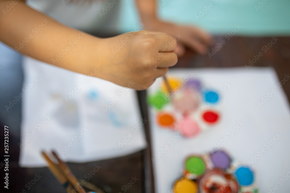 Child's hand put paint brush into used watercolor in palette on desk with background blur Child's hand put paint brush into used watercolor in palette on desk with background blur
