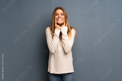 Blonde woman over grey background smiling with a happy and pleasant expression