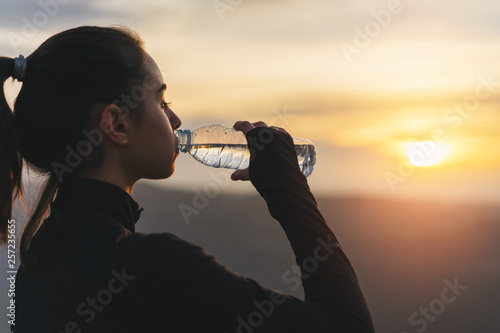 Cropped image of young sporty woman drinking water after training on the Sunset