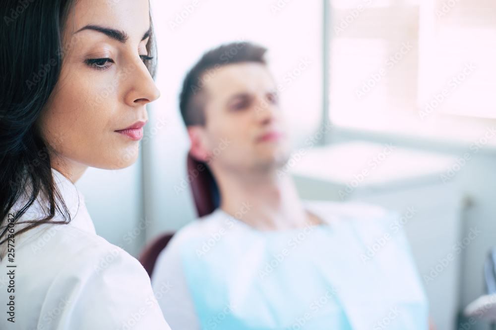 Absolute concentration. A girl clothed in a gown is working as a dentist in a clinic and concentrating on her work on a healthy teeth of her patient who is sitting in a dental chair. Absolute concentration. A girl clothed in a gown is working as a dentist in a clinic and concentrating on her work on a healthy teeth of her patient who is sitting in a dental chair.
