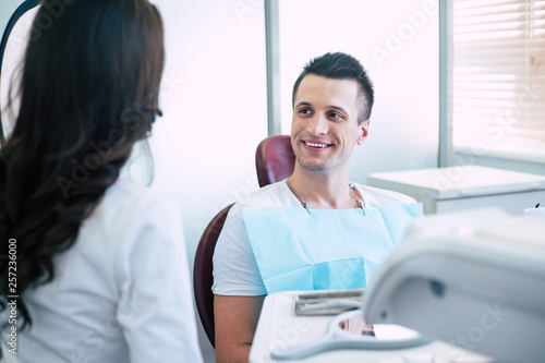 Talk turkey. A conversation between dentist and a patient who is sitting in the dental chair in front of white wall and bright lighted window and smiling because of great work of the doctor.