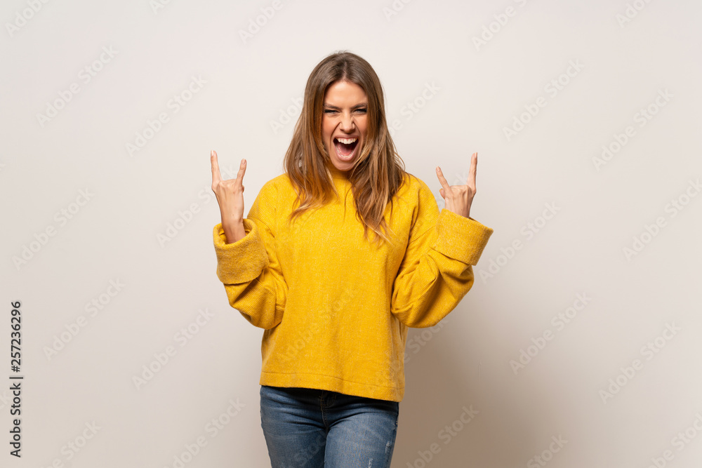 Woman with yellow sweater over isolated wall making rock gesture Woman with yellow sweater over isolated wall making rock gesture