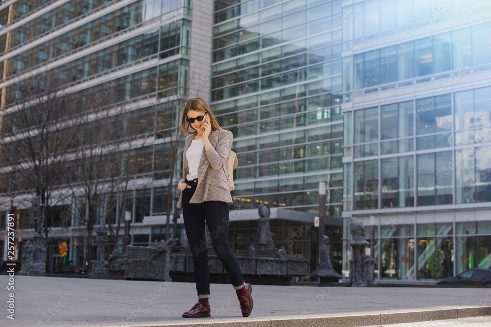 Young stylish girl talking via smartphone in downtown, Stylish blogger walking while calling her friends via smart phone