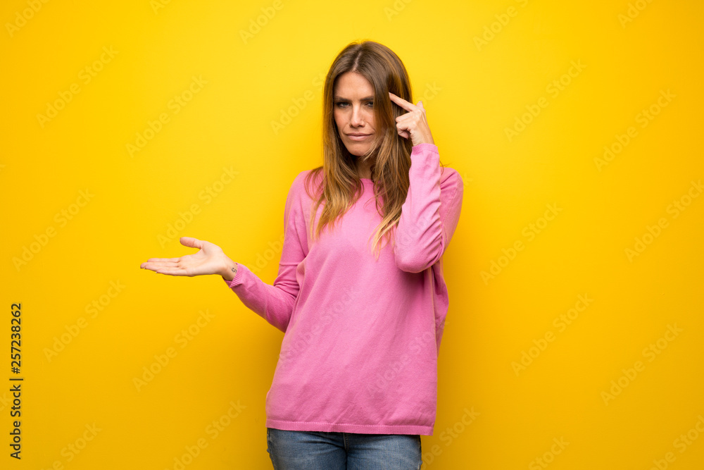 Woman with pink sweater over yellow wall making the gesture of madness putting finger on the head Woman with pink sweater over yellow wall making the gesture of madness putting finger on the head