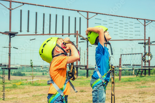 Two children in helmets and safety gear are looking up in an extreme park.