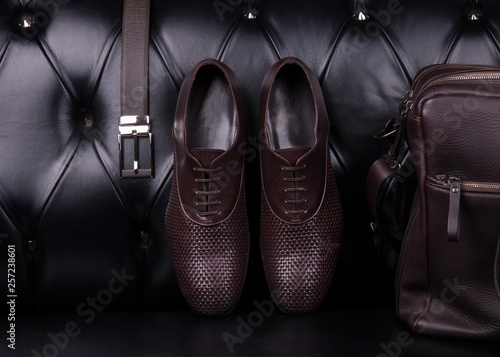 Men's fashion accessories wardrobe. Men's shoes, belt and bag against a black leather sofa.