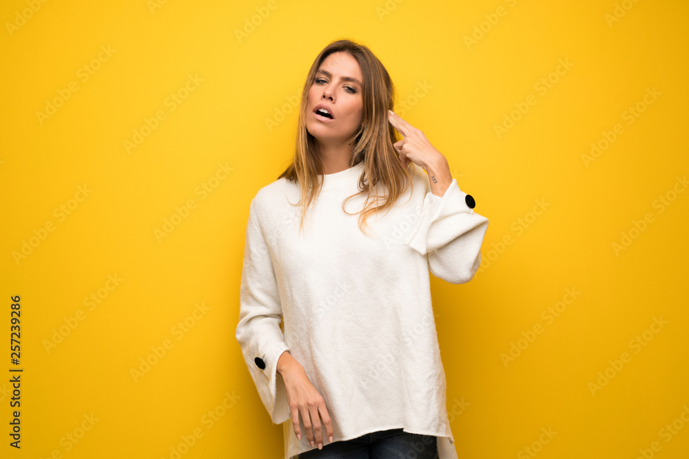 Blonde woman over yellow wall with problems making suicide gesture Blonde woman over yellow wall with problems making suicide gesture