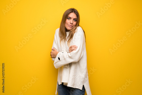 Blonde woman over yellow wall making doubts gesture while lifting the shoulders © luismolinero