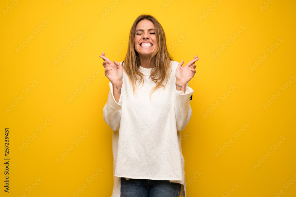 Blonde woman over yellow wall with fingers crossing and wishing the best Blonde woman over yellow wall with fingers crossing and wishing the best