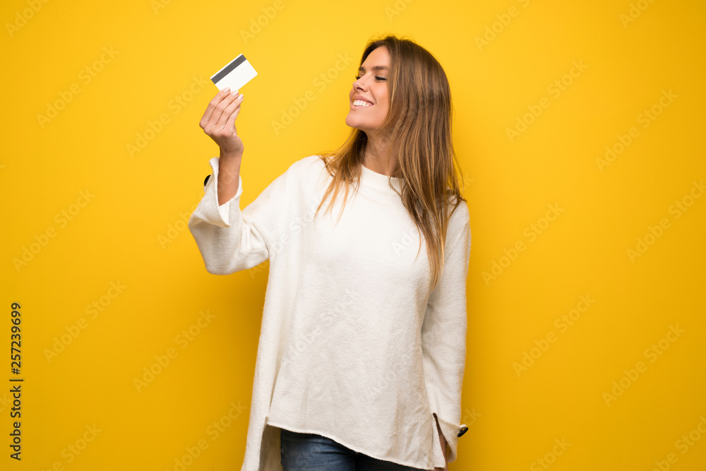 Blonde woman over yellow wall holding a credit card and thinking Blonde woman over yellow wall holding a credit card and thinking