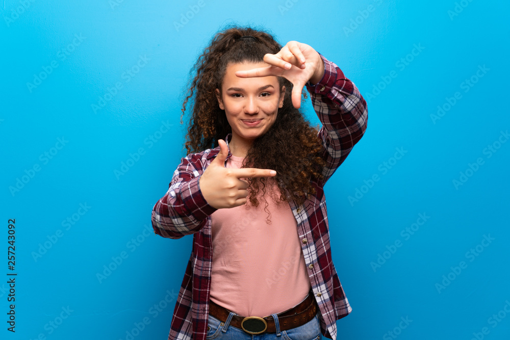 Teenager girl over blue wall focusing face. Framing symbol Teenager girl over blue wall focusing face. Framing symbol