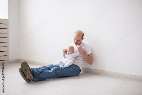 Infant, family and fatherhood concept - happy bald father holding baby daughter on knees on white background