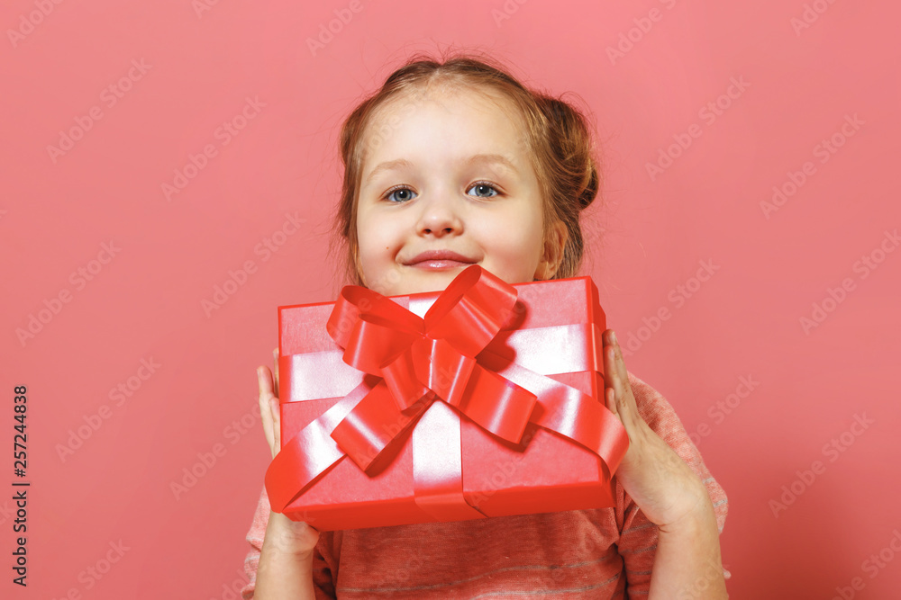 Closeup portrait of a cute little girl with buns of hair on a pink background. The child holds a box with a gift Closeup portrait of a cute little girl with buns of hair on a pink background. The child holds a box with a gift