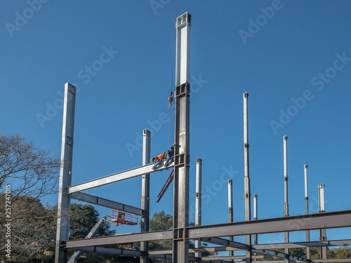 Canvas Print 2 ironworkers is straddle a horizontal steel I-beam and reach out to grab another beam to move into place