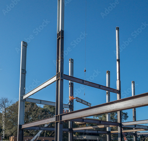 Photography An ironworker is standing on a horizontal steel I-beam and holding on to vertical I-beam waiting for an other beam to move into place