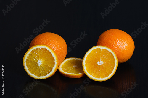 Halved and whole oranges over black background  side view. Space for text.