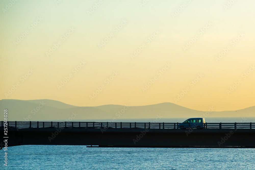 Obraz premium Cars on the highway bridge during the dawn against the backdrop of mountains and the sea