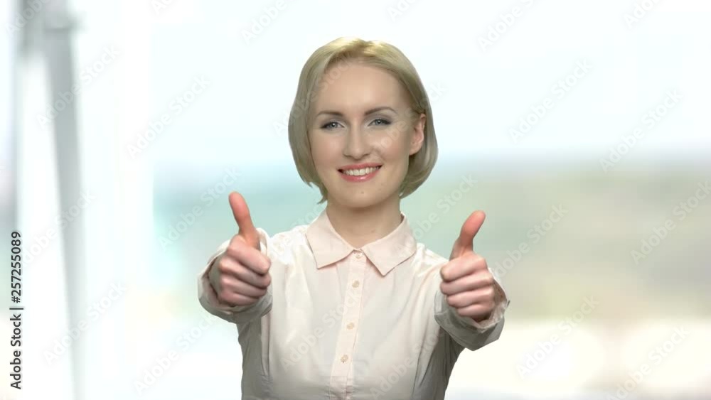 Happy business woman giving two thumbs up. Cheerful blonde woman in formal shirt gesturing thumb up with both hands. Abstract blurred background. Happy business woman giving two thumbs up. Cheerful blonde woman in formal shirt gesturing thumb up with both hands. Abstract blurred background.