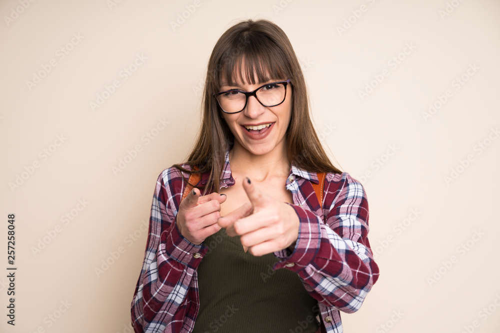 Young woman on ocher background points finger at you Young woman on ocher background points finger at you