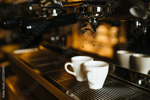 The moment of the brewing process of espresso. Coffee pours into two white cups. © Anna