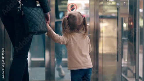 CU, 4k: Young mother leads her daughter by the hand, along the business center. They enter the elevator.