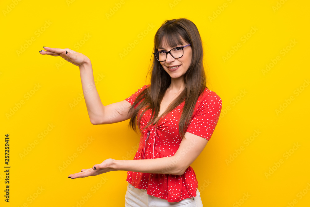Young woman over yellow wall holding copyspace to insert an ad Young woman over yellow wall holding copyspace to insert an ad