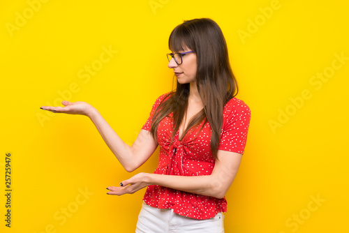 Young woman over yellow wall extending hands to the side for inviting to come © luismolinero