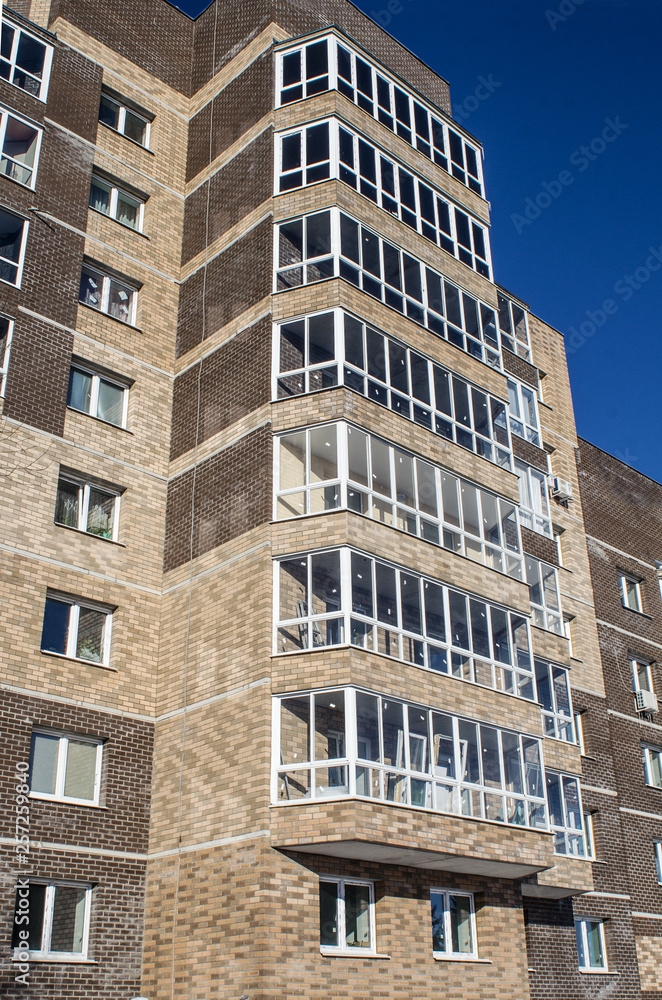 Obraz premium The new nine-storey house, illuminated by sunlight, is depicted in a sharp angle from the level of human growth against a clear sky.