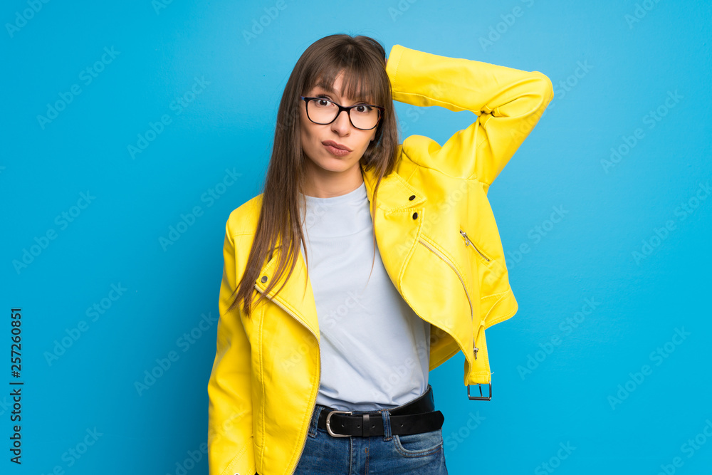 Young woman with yellow jacket on blue background with surprise and shocked facial expression