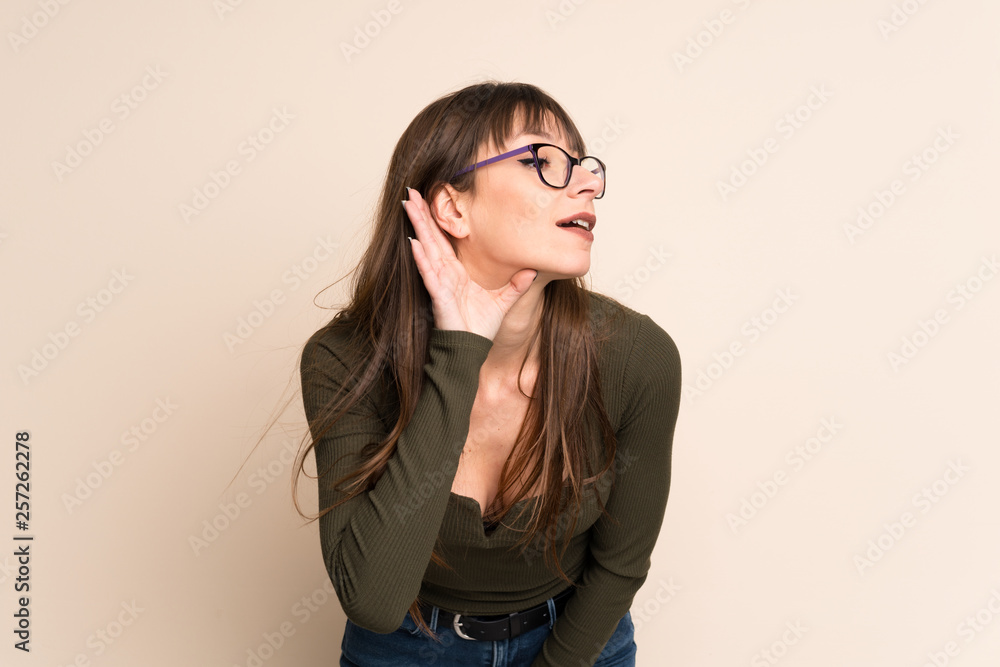 Young woman on ocher background listening to something by putting hand on the ear