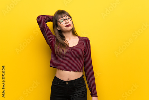Woman with glasses over yellow wall thinking an idea while scratching head