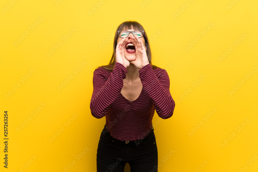 Woman with glasses over yellow wall shouting and announcing something Woman with glasses over yellow wall shouting and announcing something