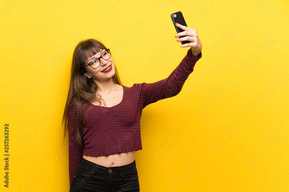 Woman with glasses over yellow wall making a selfie Woman with glasses over yellow wall making a selfie