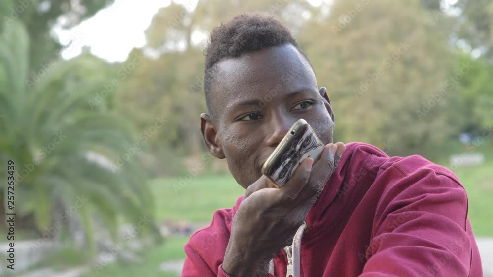 Young american african guy recording vocal message on smartphone in the park Young american african guy recording vocal message on smartphone in the park