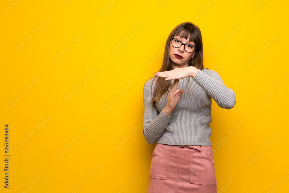 Woman with glasses over yellow wall making stop gesture with her hand to stop an act Woman with glasses over yellow wall making stop gesture with her hand to stop an act