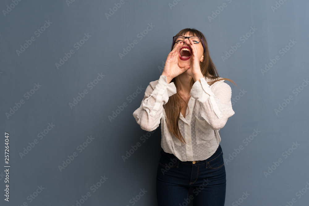 Woman with glasses over blue wall shouting and announcing something Woman with glasses over blue wall shouting and announcing something