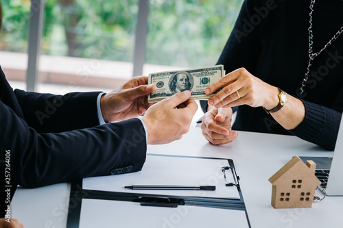 Tableau sur toile Side view of crop business people handing over dollars with decorative house mod