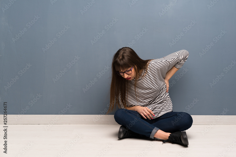 Woman with glasses sitting on the floor suffering from backache for having made an effort Woman with glasses sitting on the floor suffering from backache for having made an effort
