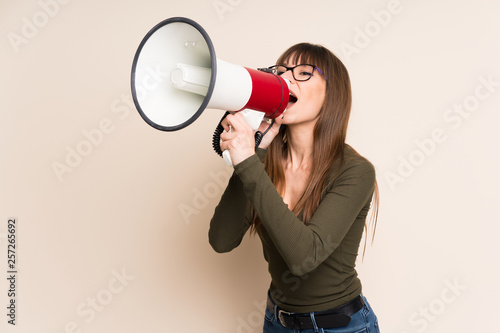 Young woman on ocher background shouting through a megaphone