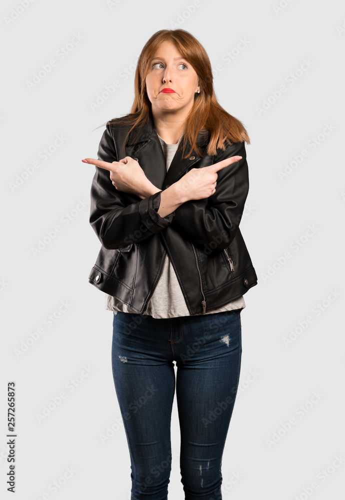 Young redhead woman pointing to the laterals having doubts over isolated grey background Young redhead woman pointing to the laterals having doubts over isolated grey background