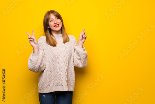 Redhead woman over yellow wall smiling and showing victory sign with both hands
