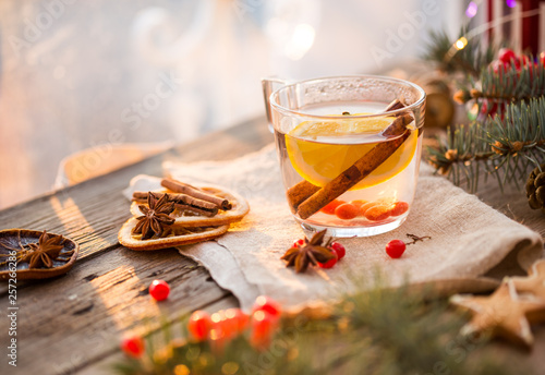 Winter theme. Christmas tea with spices, cup of tea with orange, cinnamon, anise, cookies in a shape of star, pepper and gray scarf on wooden background. Flat lay, View from above. Copy space for text photo