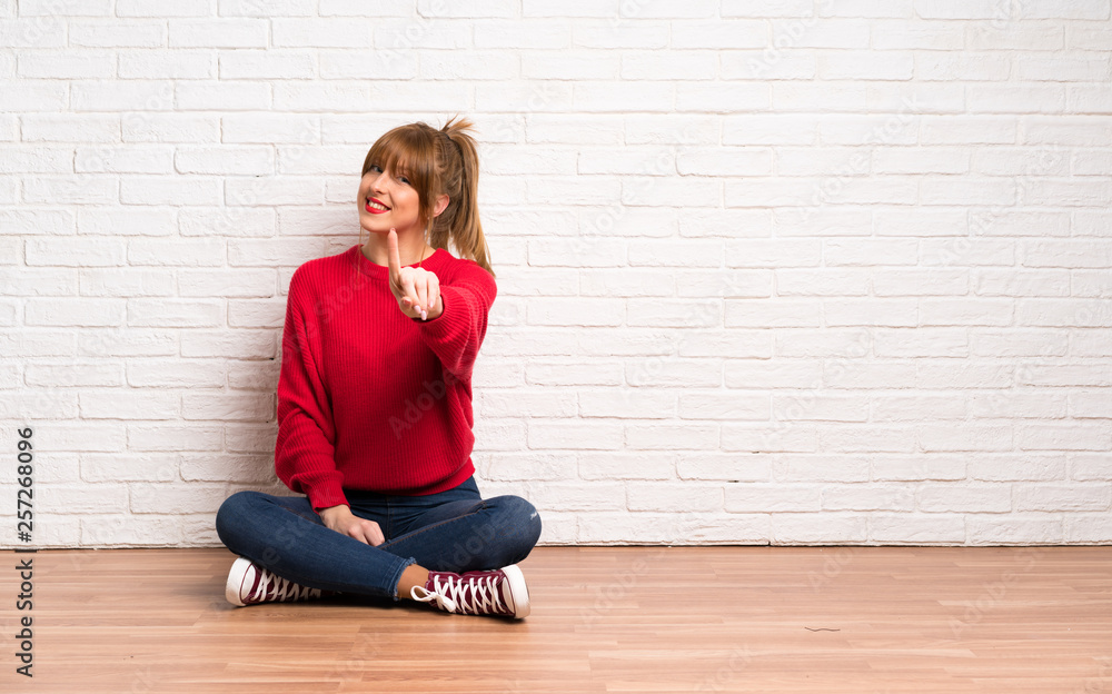 Redhead woman siting on the floor showing and lifting a finger Redhead woman siting on the floor showing and lifting a finger