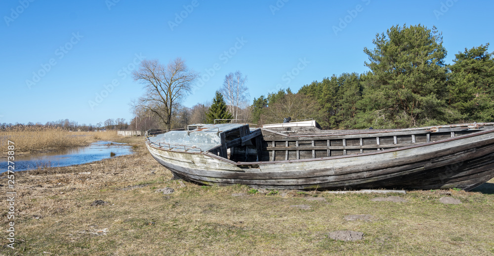 Old broken wooden fishing boat on the shore of the lake.
