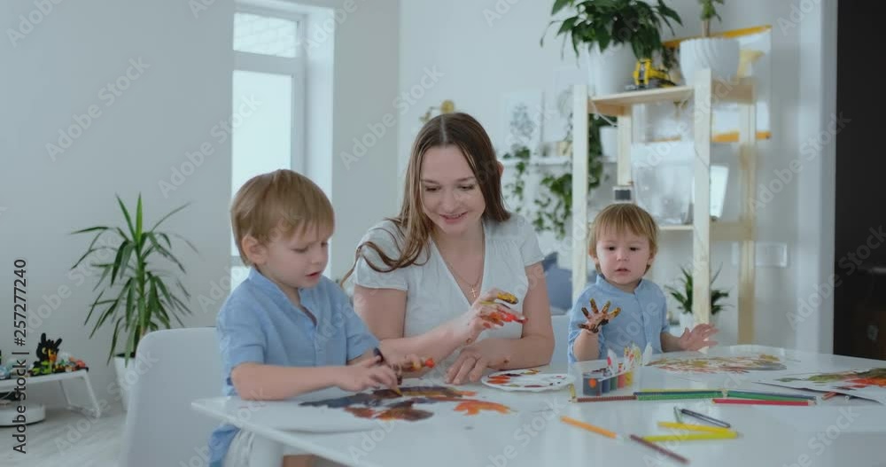 The family has fun painting on paper with their fingers in paint. Mom and two children paint with fingers on paper The family has fun painting on paper with their fingers in paint. Mom and two children paint with fingers on paper