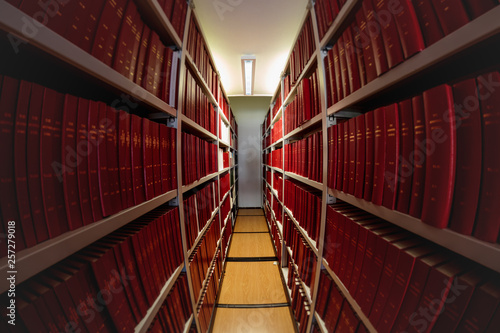Library bookshelves full of red big volume books. Distorted fisheye perspective.