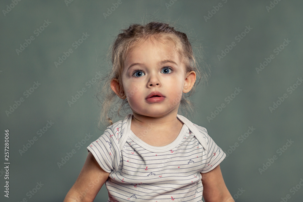 Naklejka premium Cute little girl with big blue eyes. Gray background.