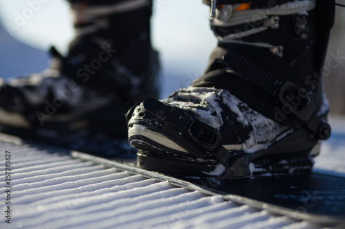 Snowboarder straps in his legs in snowboard boots in modern fast flow bindings with straps.